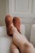 Ladies feet up wearing a pair of curly merino sheepskin slip on slipper with curls on the outside and inside in a rich, warm rust colour.
