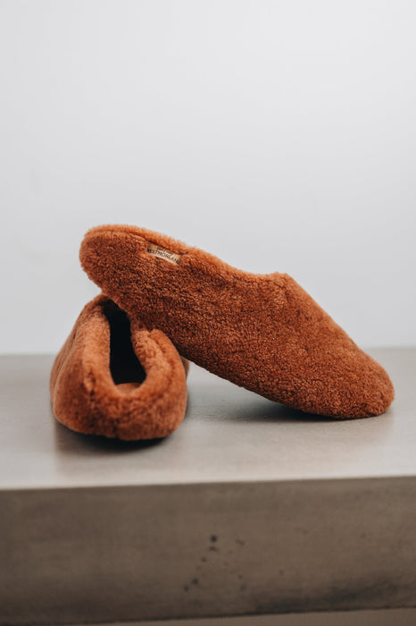 Side view of curly merino sheepskin slip on slipper with curls on the outside and inside in a rich, warm rust colour.