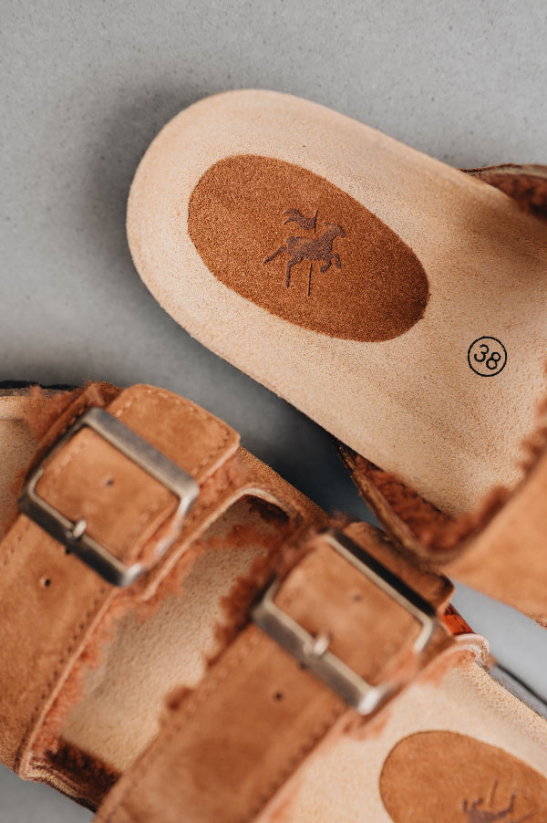 close up on the inside of the mead rust sandal with engraved branding in the soul on the sheepskin