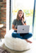 White Shorn Icelandic Sheepskin Bean Bag. Model sat cross legged on bean bag with computer.