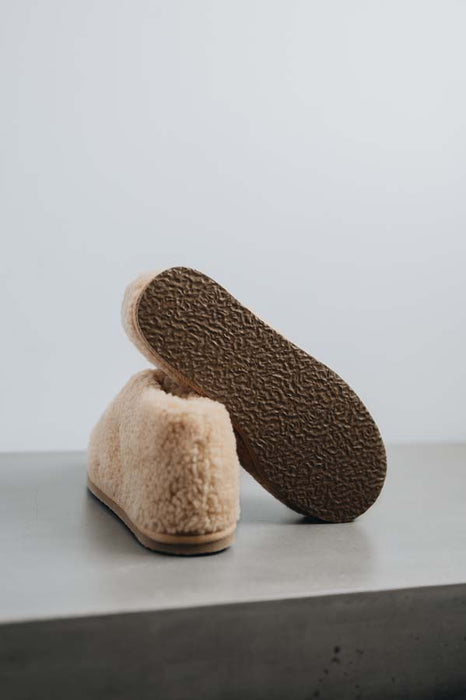 View of the underside of the rubber sole of a camel coloured curly merino sheepskin boot slipper.