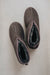 Pair of dark brown sheepskin slippers with wool lining on a light grey background
