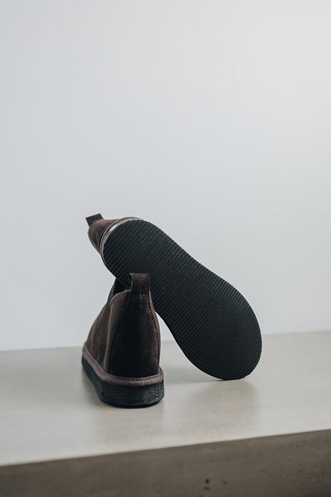 Close up of dark brown coloured ankle-high sheepskin slipper showing the ribbed underside of the PVA sole