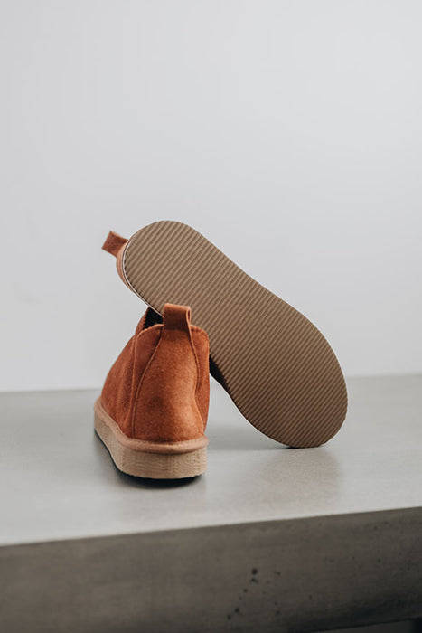 Close up of rust coloured ankle-high sheepskin slipper showing the ribbed underside of the PVA sole