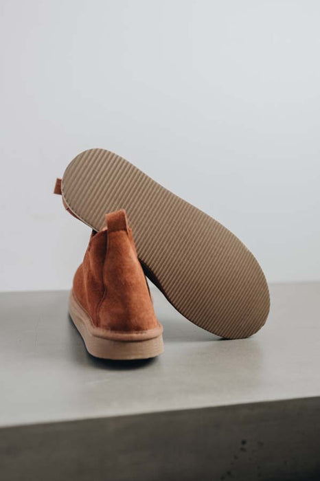 Close up of rust coloured ankle-high sheepskin slipper showing the ribbed underside of the PVA sole