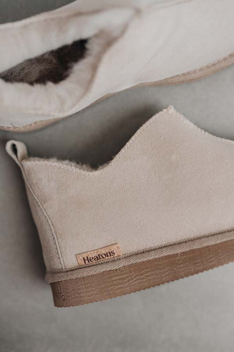 Close up of vanilla coloured ankle-high sheepskin slipper with natural cork label showing the Heatons brand