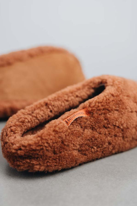 Rust curly sheepskin slip on slippers on a light grey stone background 