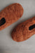 Pair of rust coloured curly sheepskin slippers on a light grey background