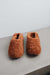 Pair of curly sheepskin rust coloured slippers on a light grey stone surface with a white background