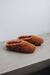 Pair of rust coloured curly sheepskin slippers on a concrete surface with a light grey background