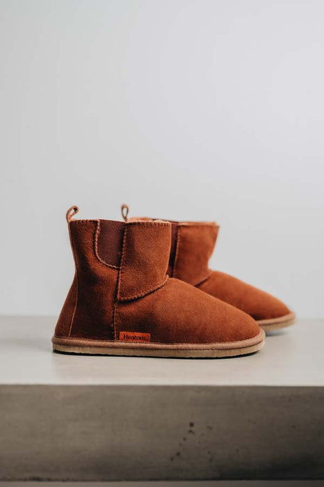 Profile view of rust coloured sheepskin boots with 8mm rubber sole on a light concrete background.