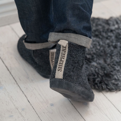 David Wool Slippers made by Shepherd of Sweden. A grey wool boot style, with a Shepherd logo beige tag at back and grey hard wearing sole. Worn by model with Navy denim trousers.