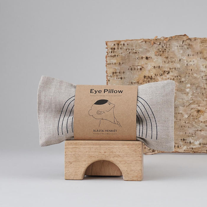 Natural white with Face design Eye Pillow. Made by Blästa Henriët. Packaged in brown cardboard informational sleeve with illustration of its use.