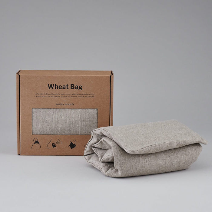 Folded Natural Plain Linen Blästa Henriët Wheat Bag. Next to it, a boxed Wheat Bag in Brown Cardboard Packaging.
