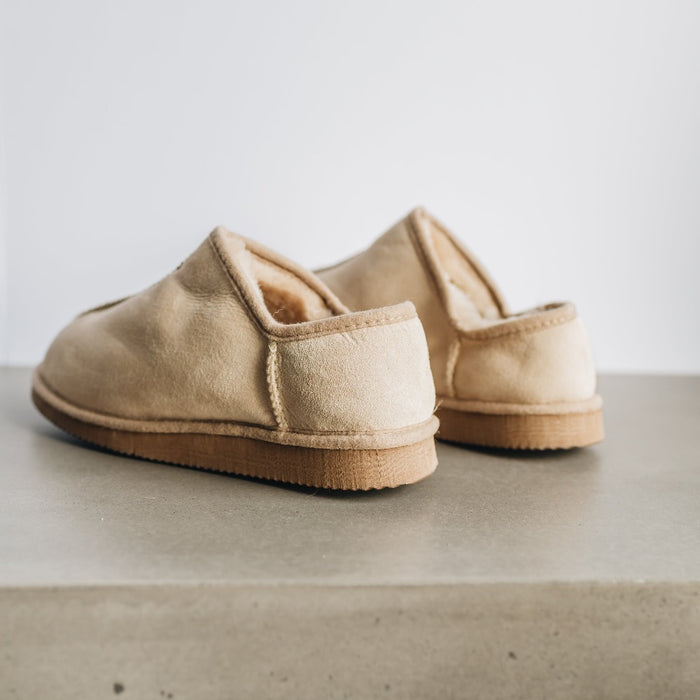 Back/side view of CADI Vanilla Sheepskin Unisex Slipper, designed by Westmorland Sheepskins. Features a small branded cork tag sewn into outer trim.