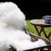 Dense wool Sheepskin British Rug in Natural White / Cream colour, dressed on deck chair with coffee table and blue mug.