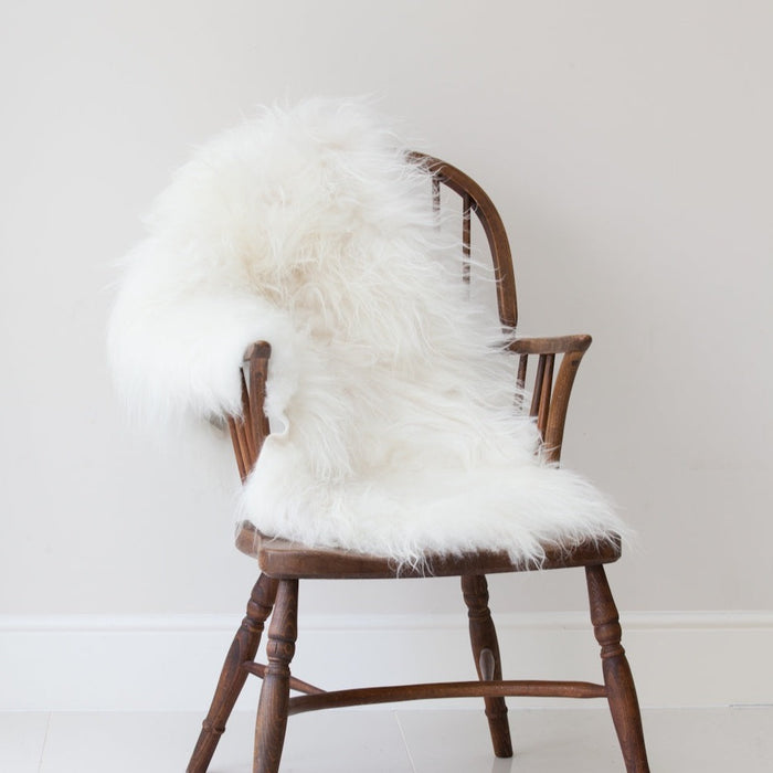 Icelandic Long Wool Sheepskin Rug in White, draped over wooden chair.