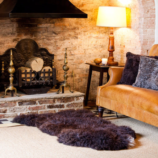 Cosy Brown British Sheepskin Rug, displayed on living room floor with accent Sheepskin cushions on leather sofa.