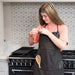Woman tying neck strap on Leather Brown Hobbyist apron with fron pockets.