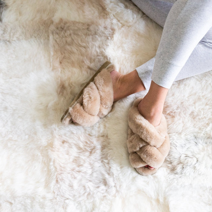 Close up of Icelandic Patchwork Designer Melange Sheepskin Rug. Shows details of the natural colour patch design. A woman's legs sit on top, featuring a pair of Gabriella Beige Women's slippers.