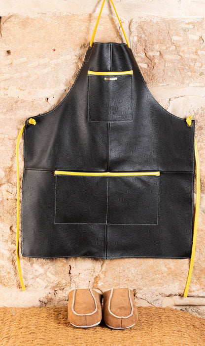 Children's Leather Apron, in black. British Leather, with Yellow accent pocket openings and tie around straps. Quality stitching and design. Featured below are a pair of Women's Sheepskin Slippers.