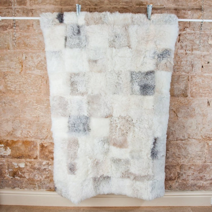 Designer White Patchwork Icelandic Sheepskin Rug, hung to show the full rug. Features grey, beige and white square patchwork design.