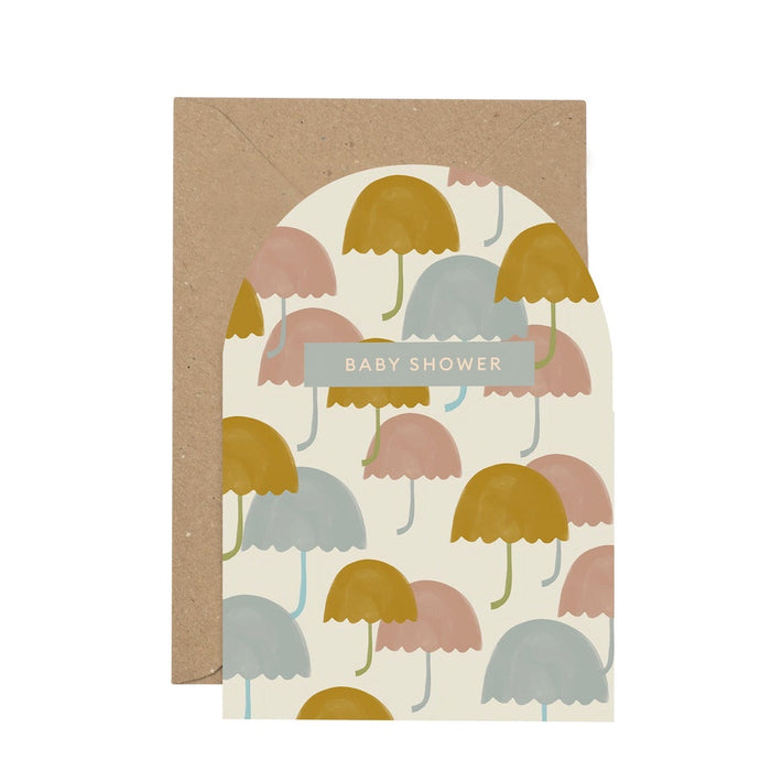 'Baby Shower' Curved Card. A white background with mustard yellow, baby blue and soft pink umbrellas dotted over the front of the card. Features a small blue rectandle with the writing 'Baby Shower'. Comes with an envelope.